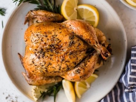 Whole roast chicken with herbs and lemon on a plate